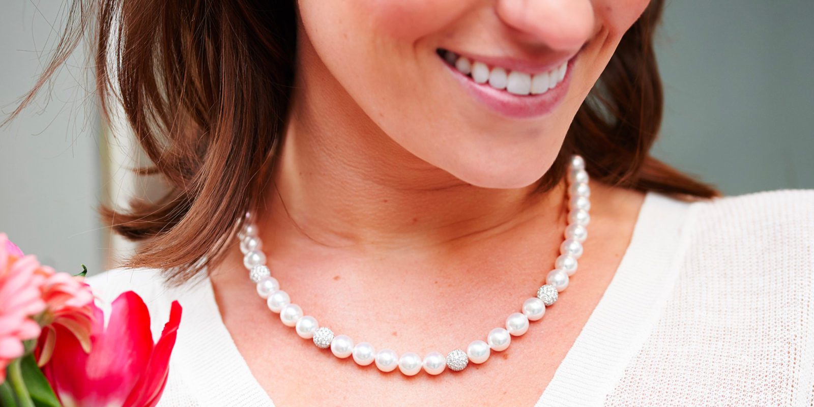 a woman wearing a pearl necklace holding a flower